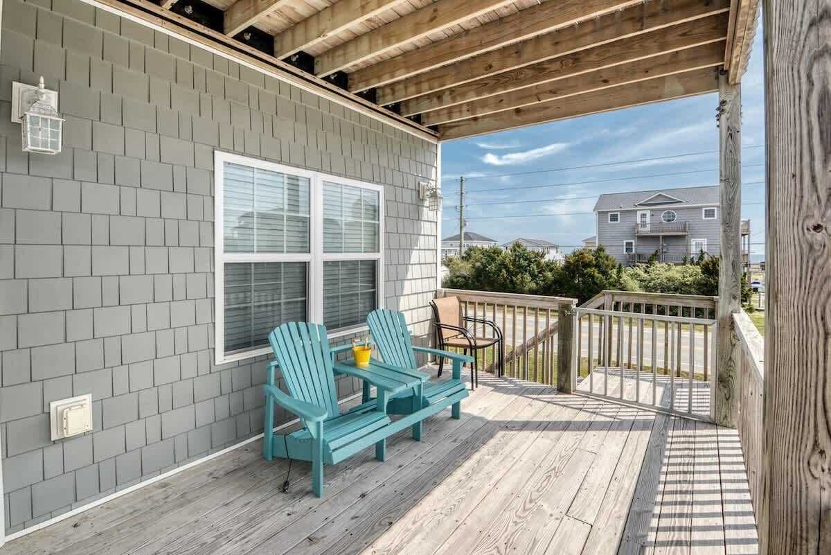 Un portico riparato con due poltrone Adirondack, un tavolino, una finestra e vista su un quartiere residenziale.