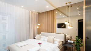 Une chambre d’hôtel moderne avec un grand lit, des tables de chevet, une plante en pot et une vue sur la ville.