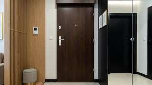 Une chambre d’hôtel moderne avec un mur lambrissé en bois, une porte en bois foncé, un petit tabouret rond et une cloison en verre.