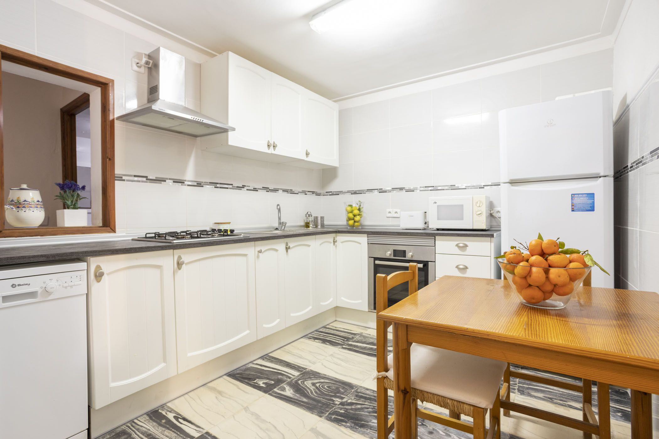 Una cocina moderna con armarios blancos, una mesa de comedor de madera y un tazón de fruta.