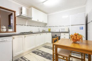 A modern kitchen with white cabinets, a wooden dining table, and a bowl of fruit. - Apartment with 3 bedrooms and 2 bathrooms on the beachfront (Alcúdia)