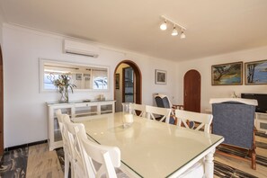 A dining area with a glass table, white chairs, a white cabinet, and a wooden door. - Apartment with 3 bedrooms and 2 bathrooms on the beachfront (Alcúdia)
