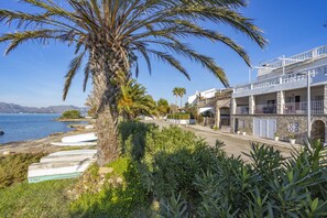 A coastal building with a balcony overlooking the sea, surrounded by greenery and palm trees. - Apartment with 3 bedrooms and 2 bathrooms on the beachfront (Alcúdia)