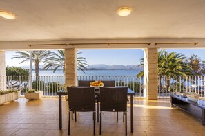 An outdoor patio with a table and chairs, a bowl of fruit, and a view of the sea and mountains. - Apartment with 3 bedrooms and 2 bathrooms on the beachfront (Alcúdia)
