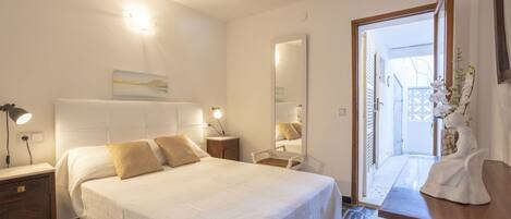 Une chambre à coucher avec un grand lit, des tables de chevet, une commode, un miroir et une vue sur l’extérieur.