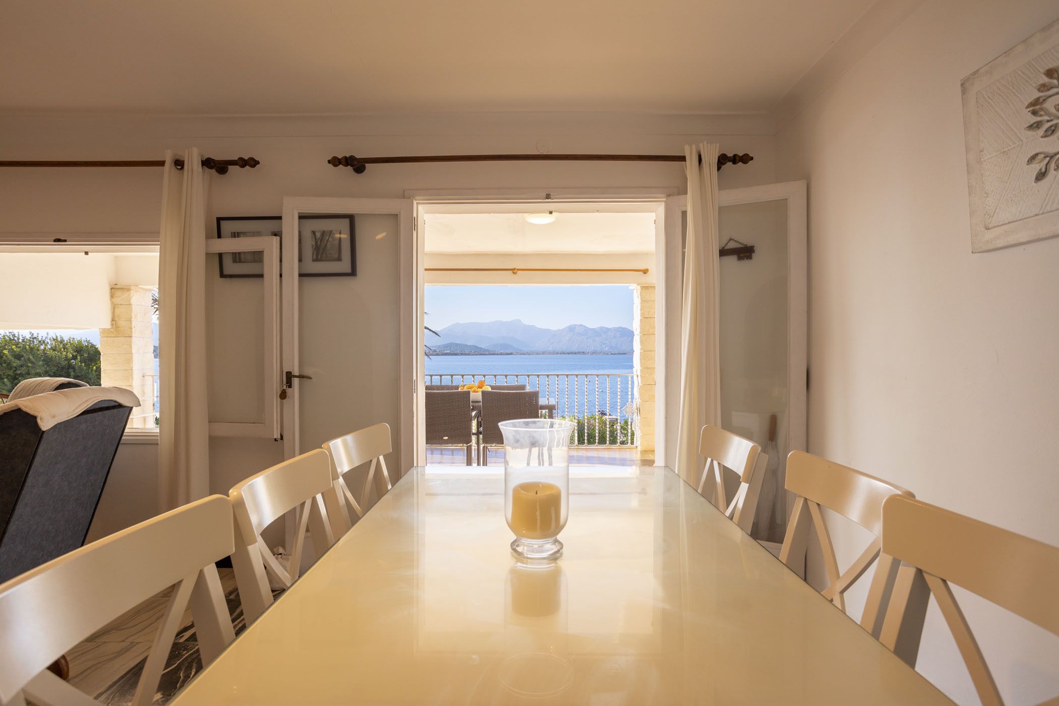 Ein Essbereich mit Tisch und Stühlen, einer Kerze und Blick auf das Meer und die Berge durch eine offene Tür.