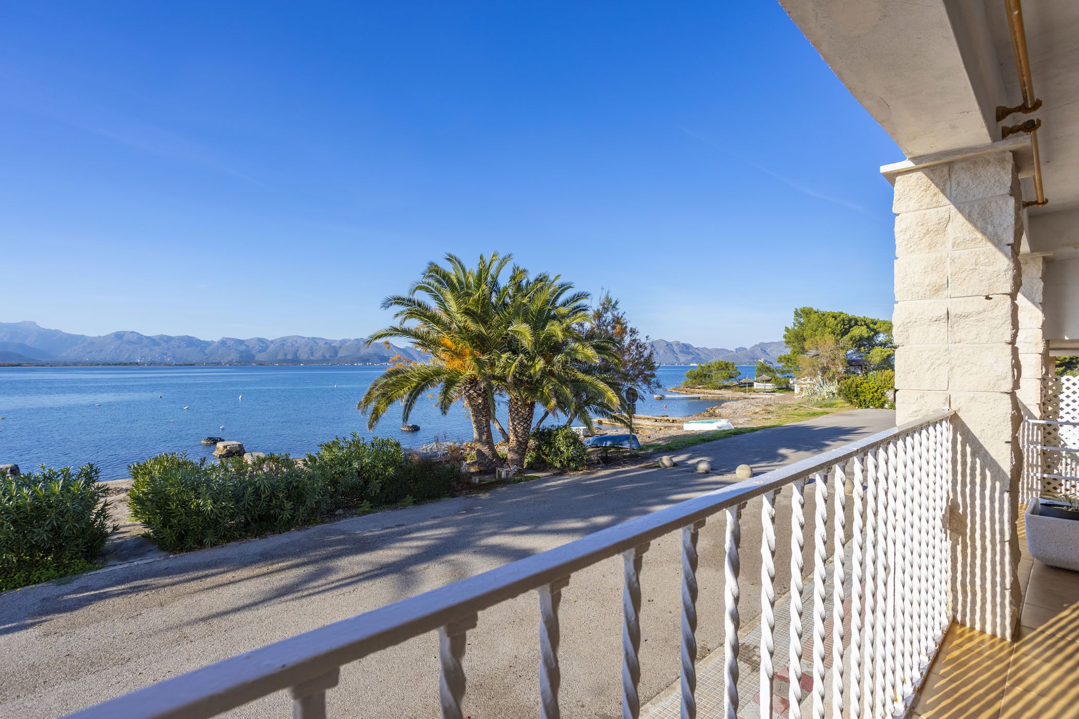 Ein Balkon mit Blick auf ein ruhiges Meer, Palmen und ferne Berge.
