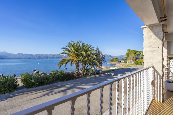 A balcony with a view of a calm sea, palm trees, and distant mountains. - Apartment with 3 bedrooms and 2 bathrooms on the beachfront (Alcúdia)