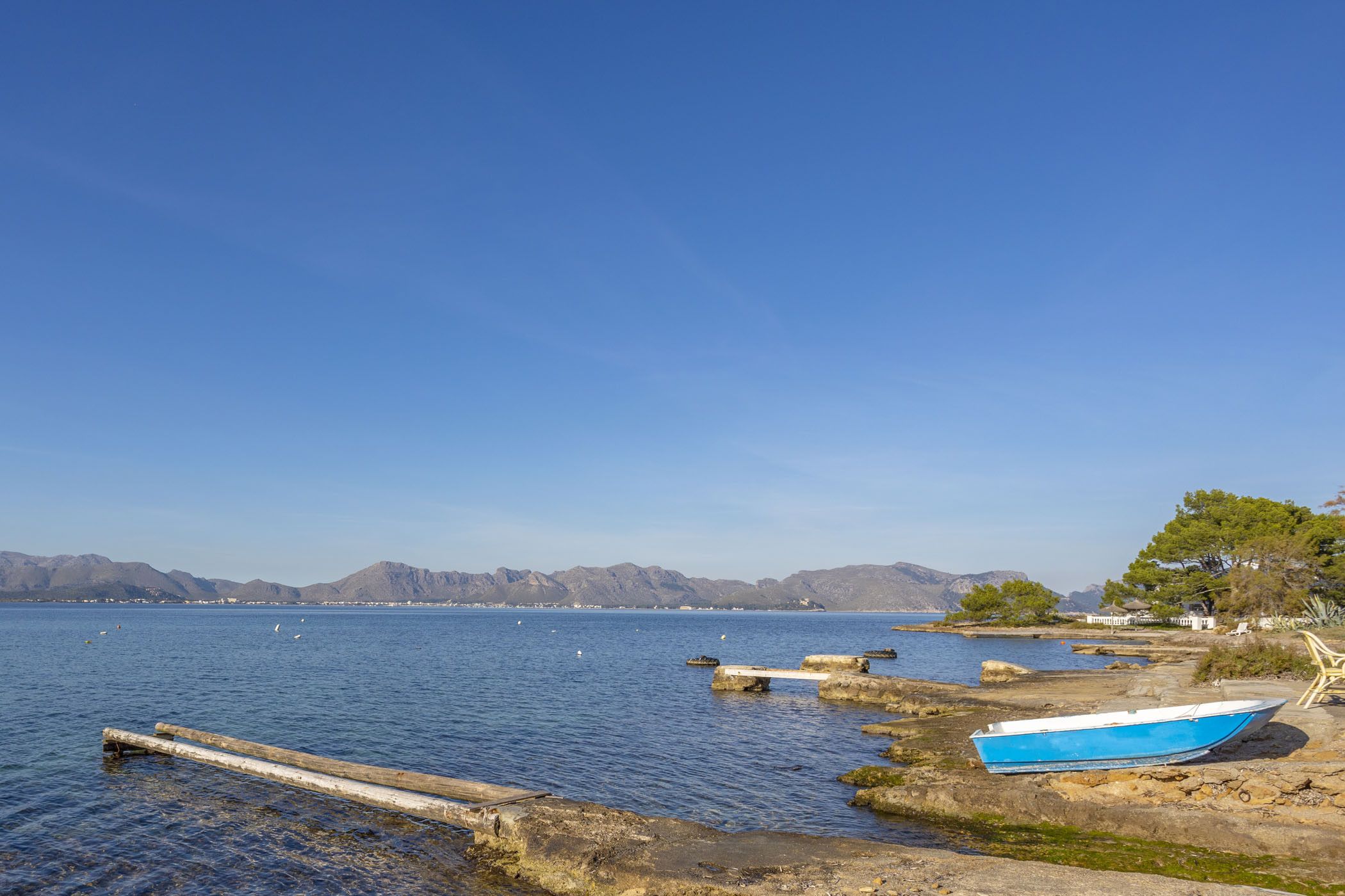 A calm lake with boats, rocky shore, and distant mountains.