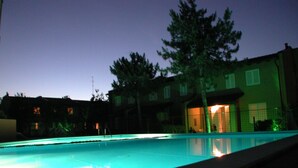 En swimmingpool med udsigt til en bygning med mange vinduer og et træ i baggrunden.