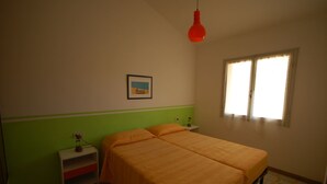 A bedroom with a bed, a nightstand, a lamp, a picture on the wall, and a window with curtains.