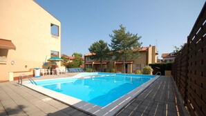 A swimming pool with lounge chairs and umbrellas, surrounded by buildings with tiled roofs.