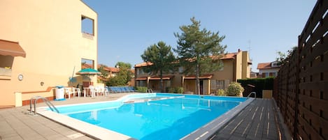 Una piscina con sillas de descanso y sombrillas, rodeada de edificios con techos de tejas.