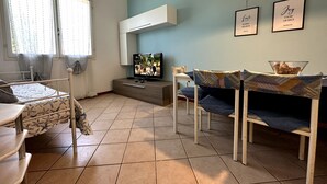 A modern living room with a TV, a dining table, and chairs. - Delta Blu Residence Village - Appartamento Quadrilocale 2 (Lido di Pomposa)
