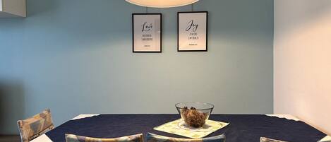 Un coin repas avec une table, des chaises et deux citations encadrées accrochées au mur.