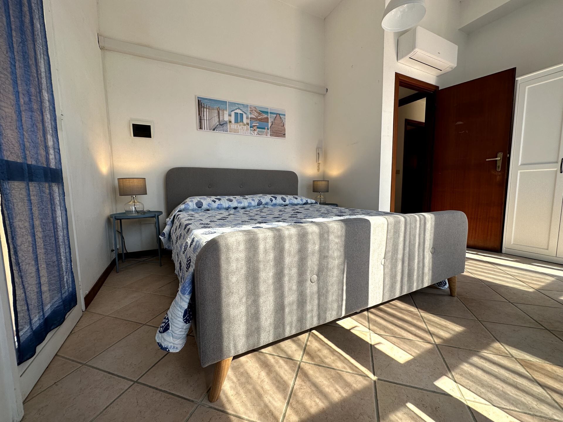 Een slaapkamer met een bed, nachtkastje, wandlamp, deur en raam met gordijnen.