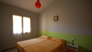 A bedroom with two beds, a window with curtains, a bedside table with a lamp, and a wall-mounted picture.