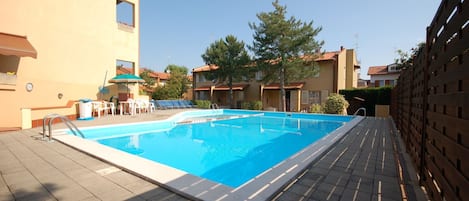 Una piscina con solárium empedrado, rodeada de edificios con balcones y un cielo despejado.