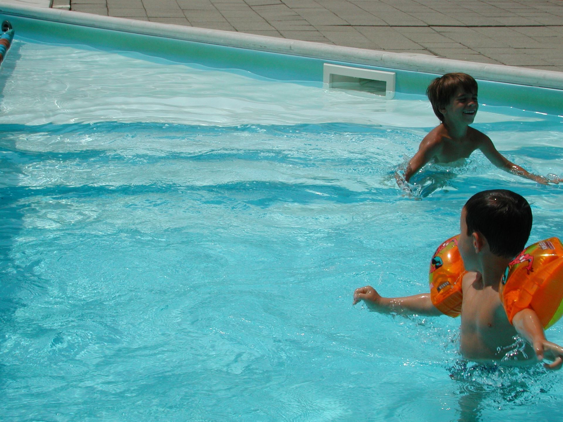 A swimming pool with clear blue water and a tiled deck surrounding it.