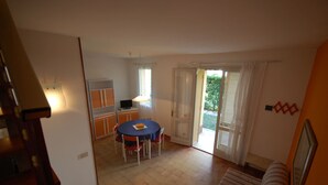 Une pièce compacte comprenant une table à manger, des chaises, un petit coin cuisine et une porte-fenêtre coulissante donnant sur un espace extérieur.