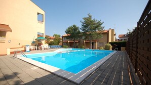 A swimming pool with a tiled deck, surrounded by buildings with balconies and a clear sky. - Delta Blu Residence Village - Villetta Trilocale 19 (Lido di Pomposa)
