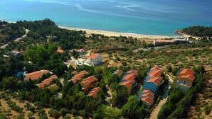 An aerial view of a coastal resort with multiple buildings, a beach, and a clear view of the sea. - Tripiti Bungalows (Thasos)