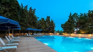 A swimming pool with lounge chairs and umbrellas, surrounded by trees. - Tripiti Bungalows (Thasos)