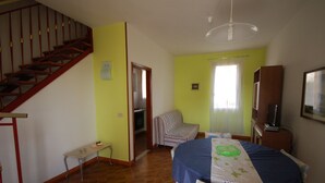 A bedroom with a bed, a chair, a table, a staircase, and a door leading to a kitchen. - Delta Blu Residence Village - Villetta Trilocale 22 (Lido di Pomposa)