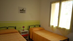 A room with two single beds, a nightstand with a lamp, a window with curtains, and a framed picture on the wall. - Delta Blu Residence Village - Villetta Trilocale 22 (Lido di Pomposa)