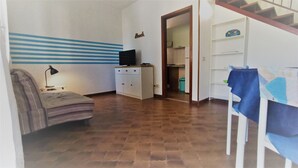 A room with a bed, a TV on a cabinet, a desk with a lamp, and a staircase.