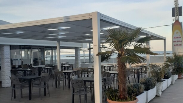 An outdoor seating area with tables and chairs, a covered section, and potted plants.