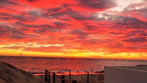 A beach with a sunset and a wooden fence in the foreground.