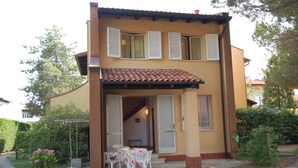 A two-story house with a tiled roof, a balcony, and a small patio area with a table and chairs. - Delta Blu Residence Village - Villetta Trilocale 10 (Lido di Pomposa)