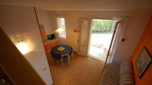 A compact living space with a dining area, a television, and a sliding glass door leading to an outdoor area. - Delta Blu Residence Village - Villetta Trilocale 10 (Lido di Pomposa)