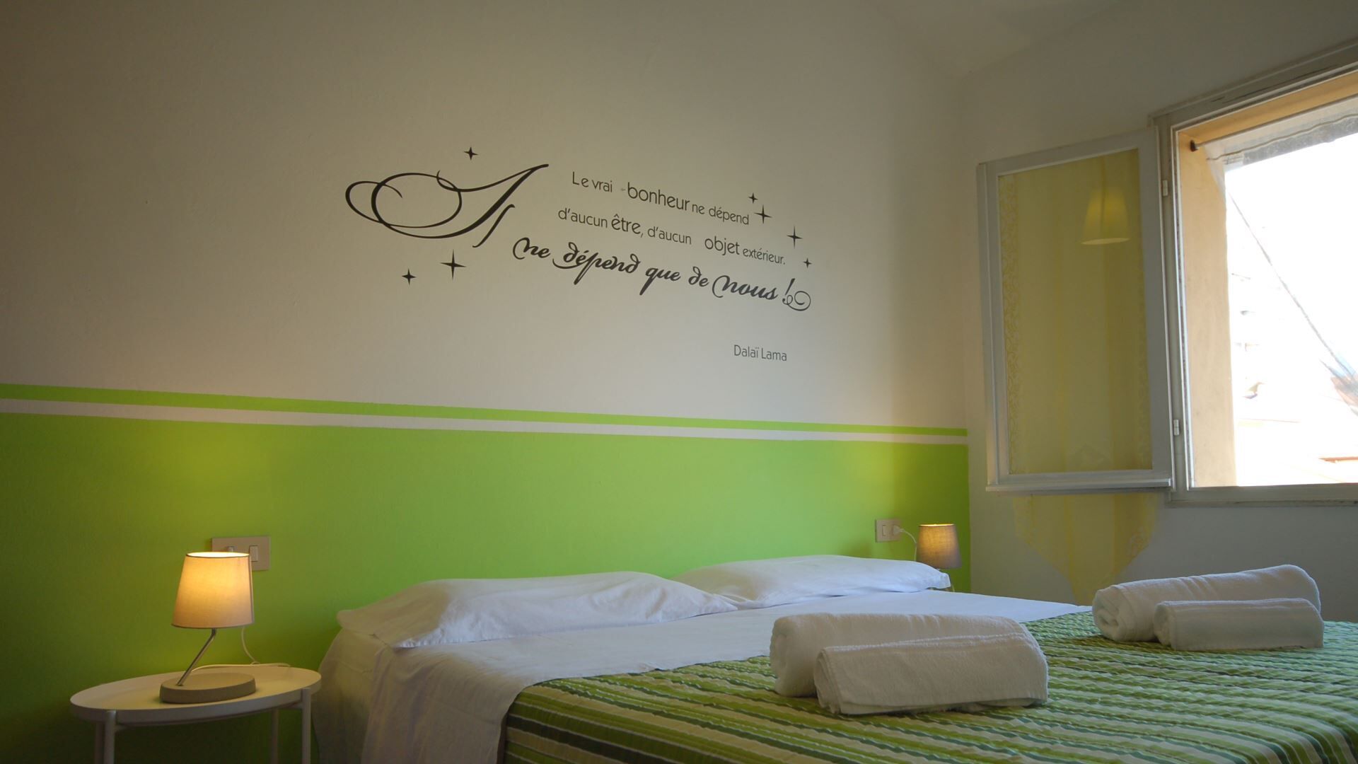 Habitación de hotel con una cama, dos lámparas de noche, una pared con una cita motivacional y una ventana.
