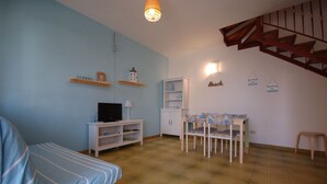 Een gezellige woonkamer met een bank, een televisie, een boekenkast, een eettafel met stoelen en een trap.