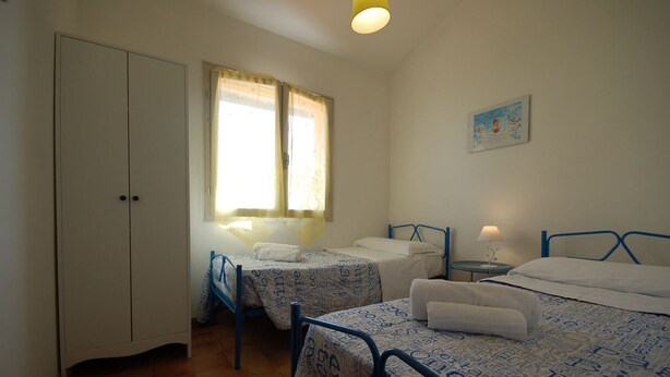 Une chambre avec deux lits simples, une armoire, une fenêtre avec des rideaux et un tableau au mur.