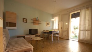 Un soggiorno con divano, televisore e zona pranzo con sedie e tavolo.