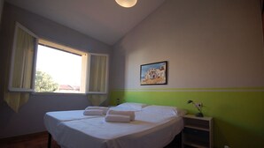 Una camera da letto con due letti, una finestra con tende, un quadro appeso al muro e un comodino con una lampada.