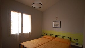 Een slaapkamer met een bed, een raam met gordijnen, een nachtkastje met een lamp en een lijst met een afbeelding aan de muur.