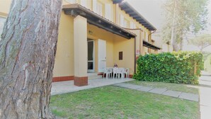 Um edifício com varanda coberta, porta branca e uma pequena mesa com cadeiras.