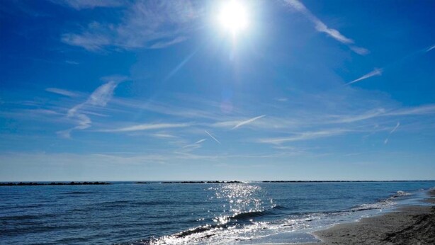 Uma praia com céu limpo e luz do sol refletindo na água.