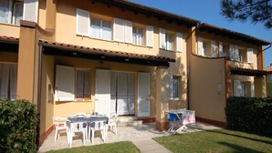A two-story building with a tiled roof, white shutters, and a covered patio area with a table and chairs.