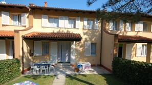 Ein zweistöckiges Gebäude mit einem Ziegeldach, zahlreichen Fenstern mit Fensterläden und einer überdachten Terrasse mit Gartenmöbeln.