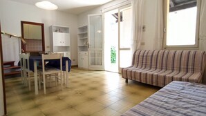 A room with a dining table, chairs, a striped sofa, a bed, and a sliding glass door leading to a balcony.