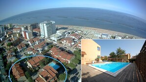 An aerial view of a coastal city with a beach, residential buildings, and a swimming pool.