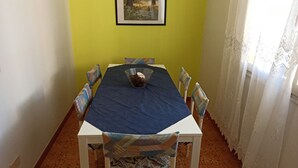 A dining area with a table set for six, chairs with patterned upholstery, a framed picture on the wall, and a window with sheer curtains.