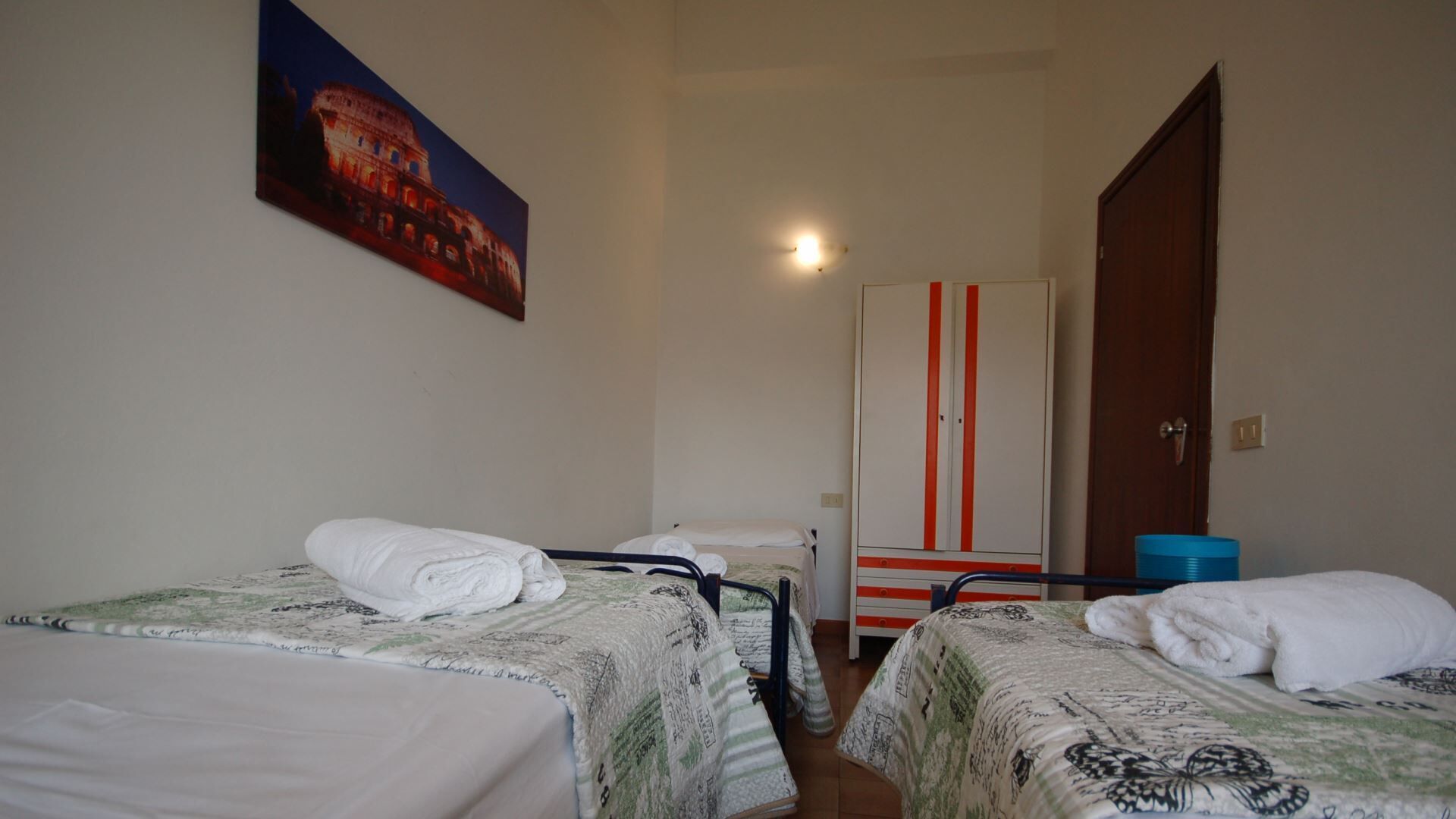 Ein Hotelzimmer mit zwei Einzelbetten, einem Kleiderschrank und einem Gemälde eines historischen Gebäudes.