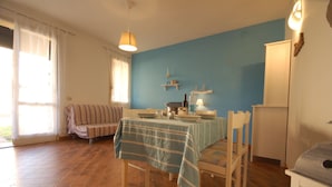 Une pièce comprenant une table à manger dressée pour deux personnes, un canapé, un meuble et une fenêtre avec des rideaux.