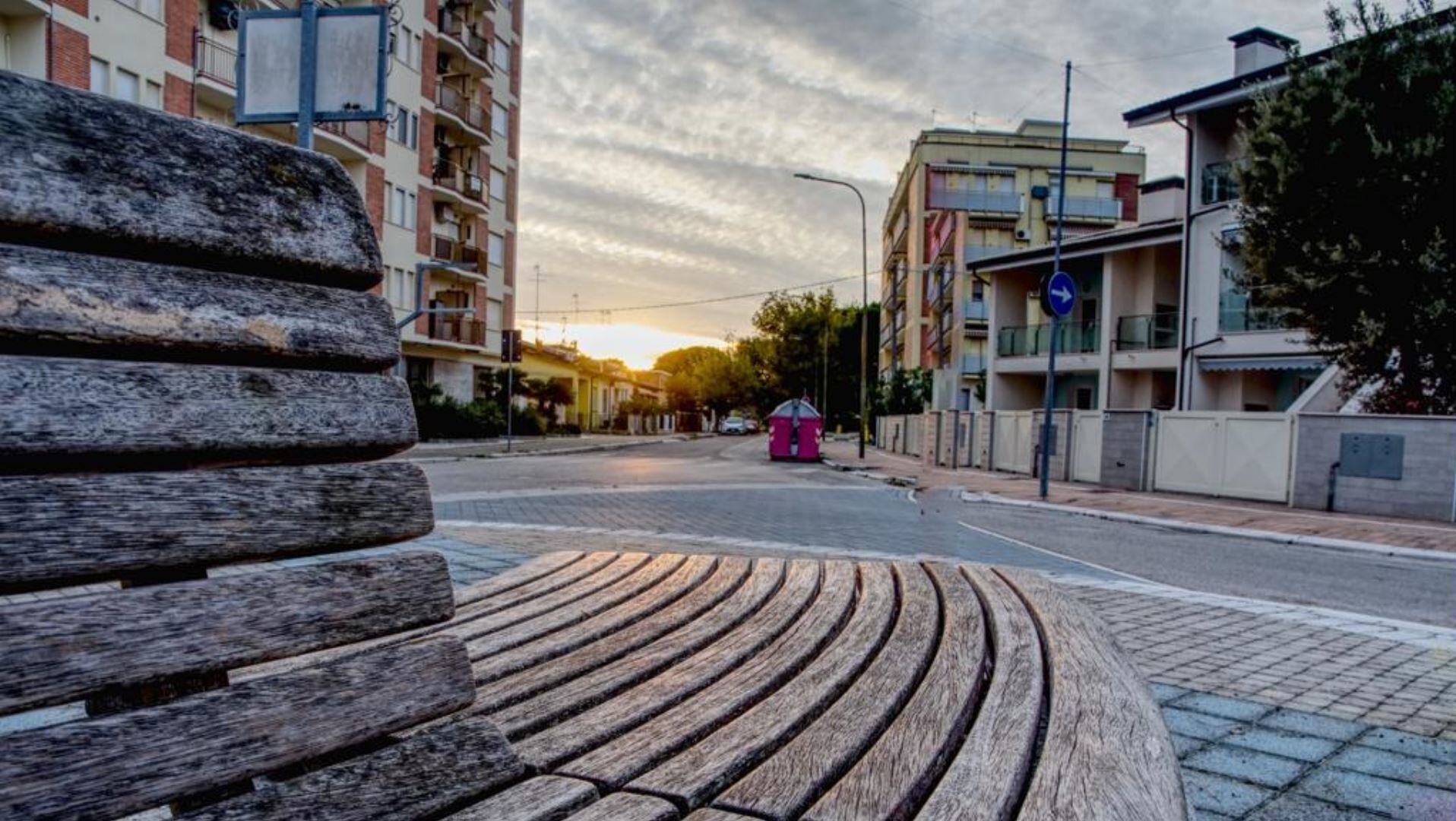 Una banca de disseny corbat, un carrer amb edificis i un tramuntana al fons.